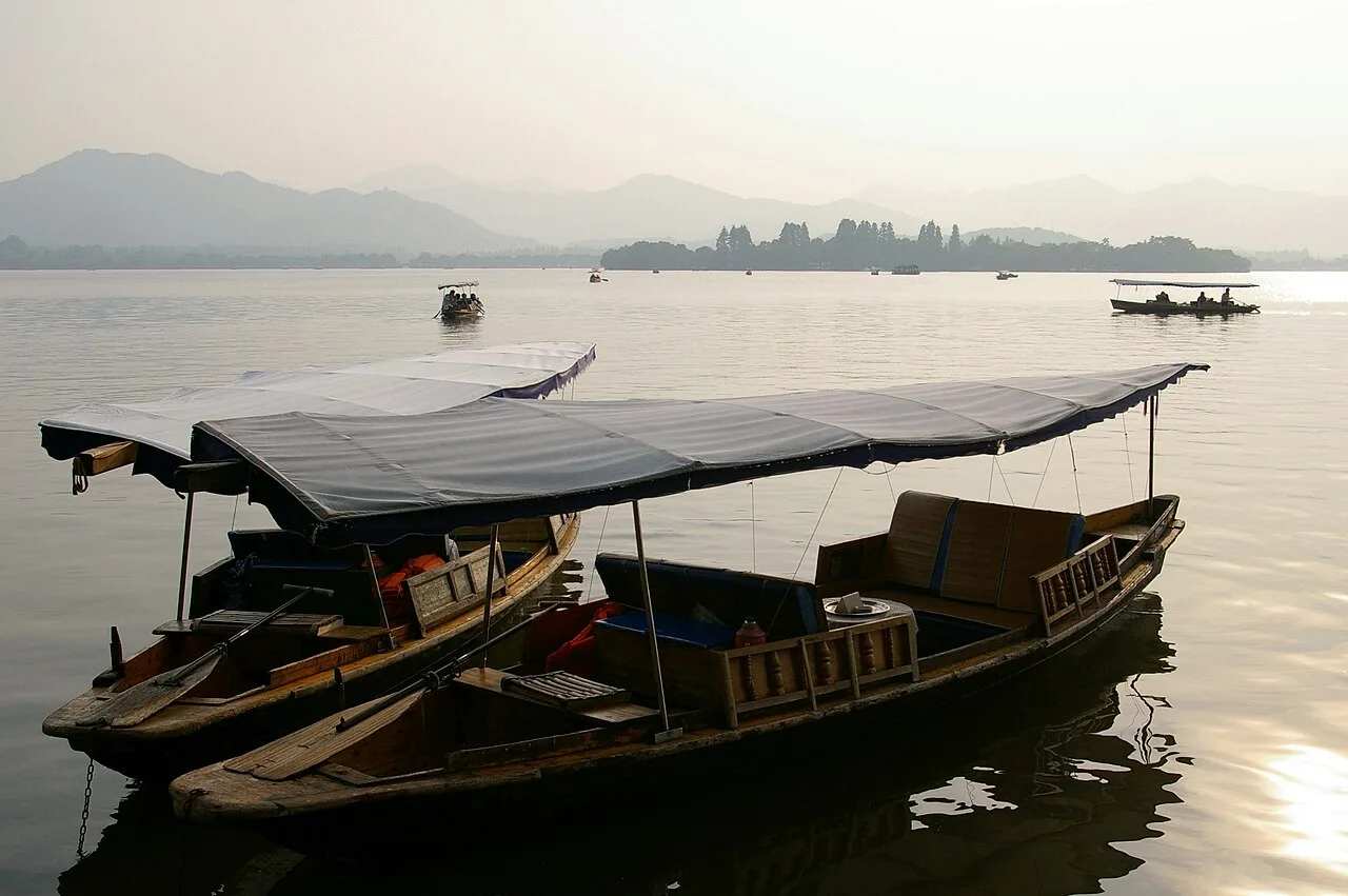 Traditional boats on West Lake with low hills in the distance